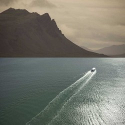 A ferry crosses an expanse of sea towards distant mountains in this photo based artwork by Mark Bartkiw.