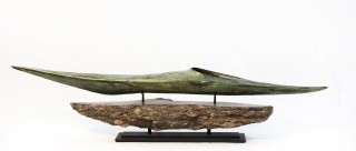 A bronze sea kayak patinated in an elegant green and gold is mounted on a granite base.