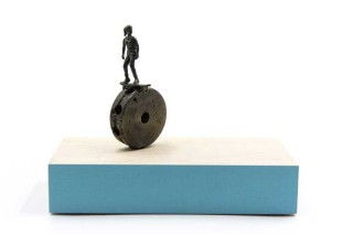 A skateboarder rides a tinkertoy wheel in this playful bronze and wood sculpture by P.