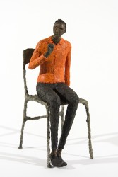 A seated figure in a orange waits quietly in this contemplative paper mache sculpture by Paul Duval.